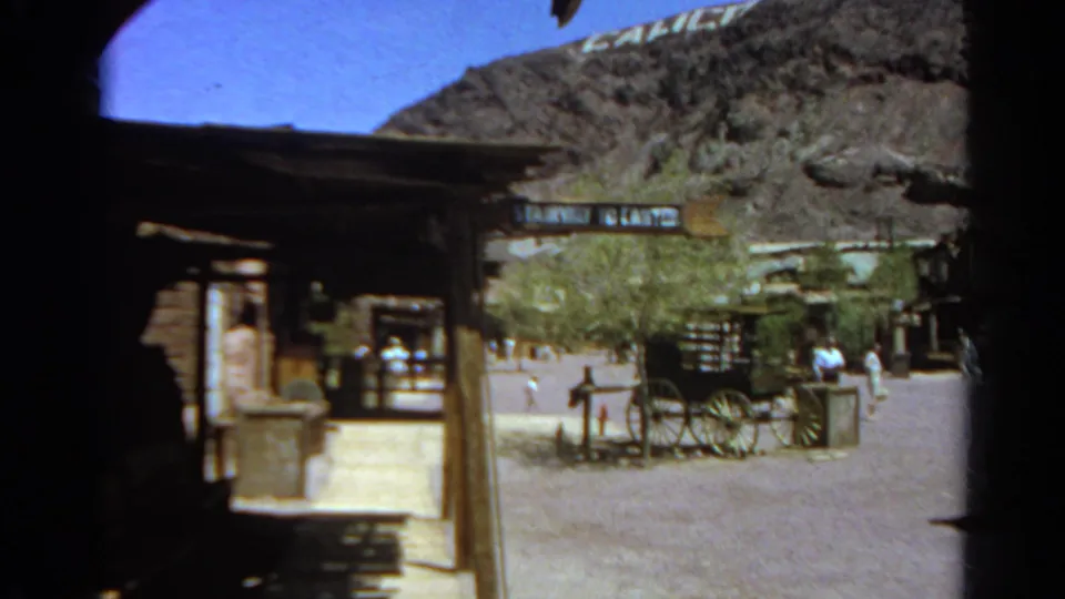 1966 Silver Lake-area home-movie view of a rustic courtyard with a horse-drawn wagon, shaded structures, distant visitors, and partial hillside lettering.
