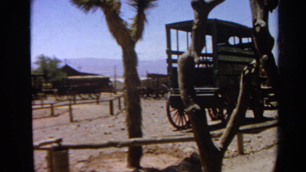 1966 Silver Lake 8mm frame showing a wooden carriage, Joshua tree form, low fencing, and hazy hills beyond.