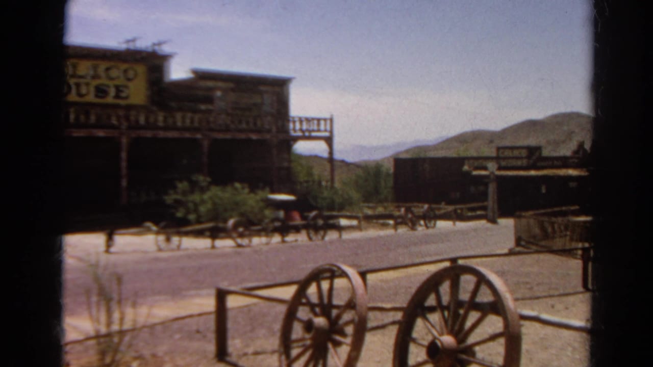 1966 8mm frame with a readable Calico House sign, wooden balcony, wagon wheels, street frontage, and arid hills.