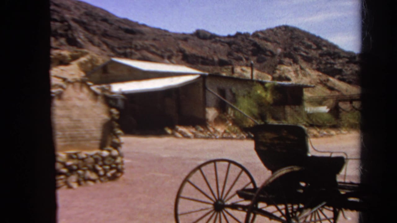 Wagon and weathered buildings seen against rocky hills.