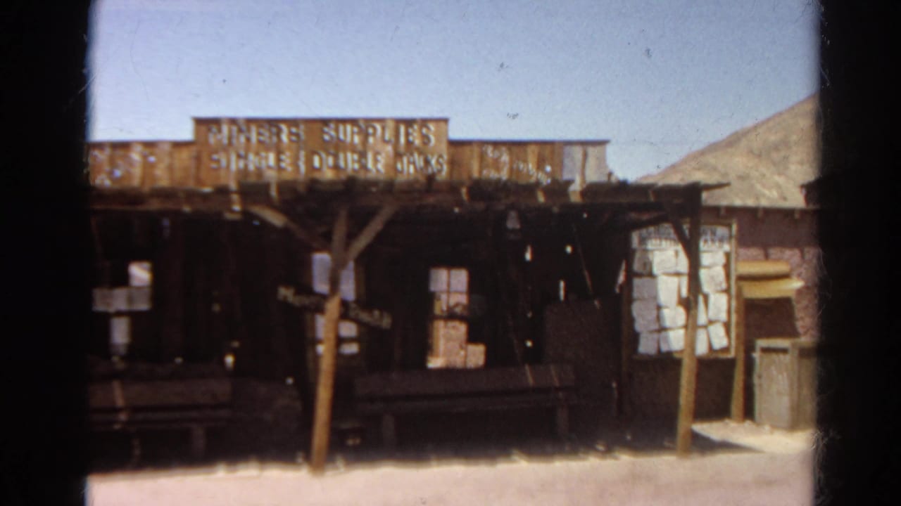 Weathered wooden storefront with miners supplies signage in a dusty Western town setting.