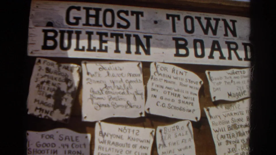 Close view of a ghost town bulletin board with painted wood lettering and handwritten notices, filmed in Silver Lake, California in 1966.