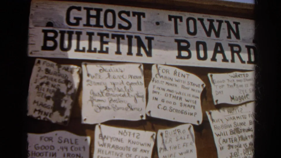 1966 8mm close-up of the ghost town bulletin board, showing handwritten sale, rent, and wanted-style notices on weathered wood.