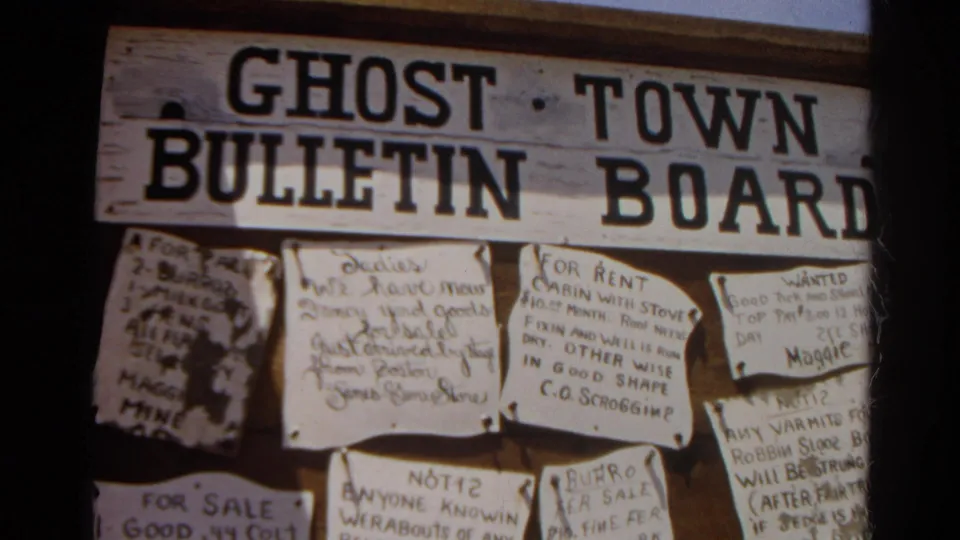 Final 1966 Silver Lake frame centered on the ghost town bulletin board, with pinned paper notices and bold painted lettering.