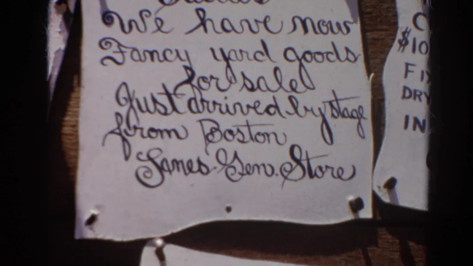 Silver Lake 1966 home-movie frame centered on a curled handwritten sale notice pinned to a wooden ghost town display.