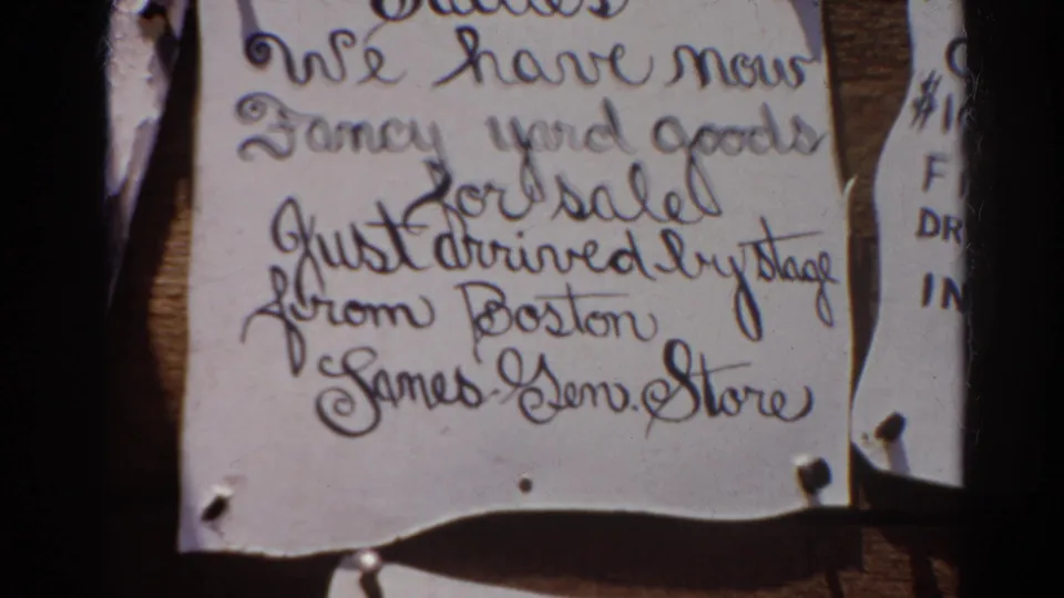 Soft 8mm close-up of the ghost town display notice, with handwritten sale text, tack marks, and warm faded color.