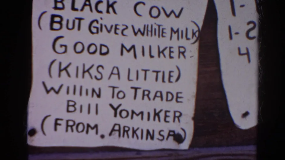 Close-up of a 1966 Silver Lake 8mm frame showing a handwritten sign about a black cow, white milk, and a possible trade.