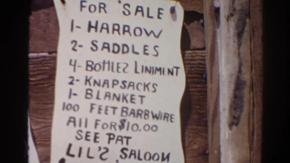 1966 Silver Lake home-movie frame of the second pinned sale sign, showing western-style goods, a $10.00 total, and handwritten Lil' 2 Saloon lettering.