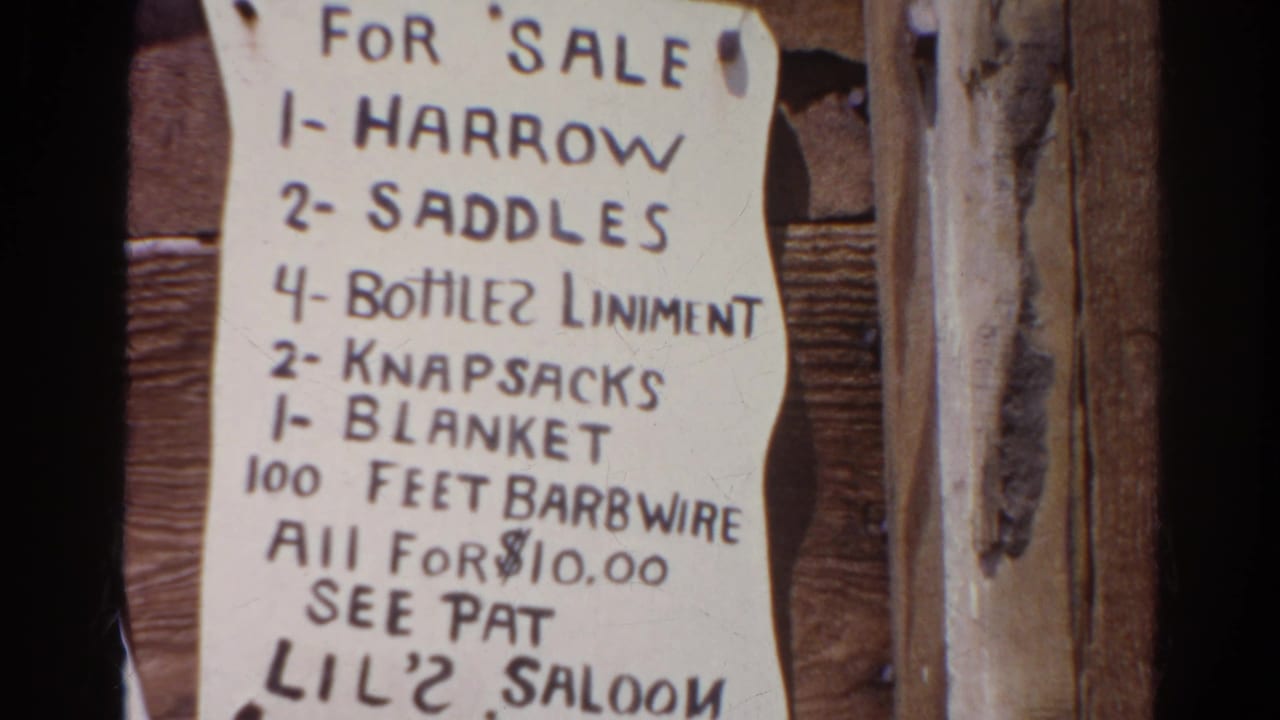 1966 Silver Lake 8mm frame showing a handwritten sale notice for saddles, knapsacks, a blanket, and barbed wire on rough boards.