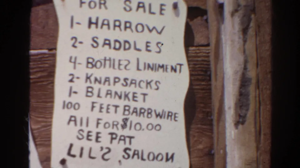 Close 8mm view of a paper sign listing a harrow, saddles, liniment, knapsacks, blanket, and barbed wire for sale.