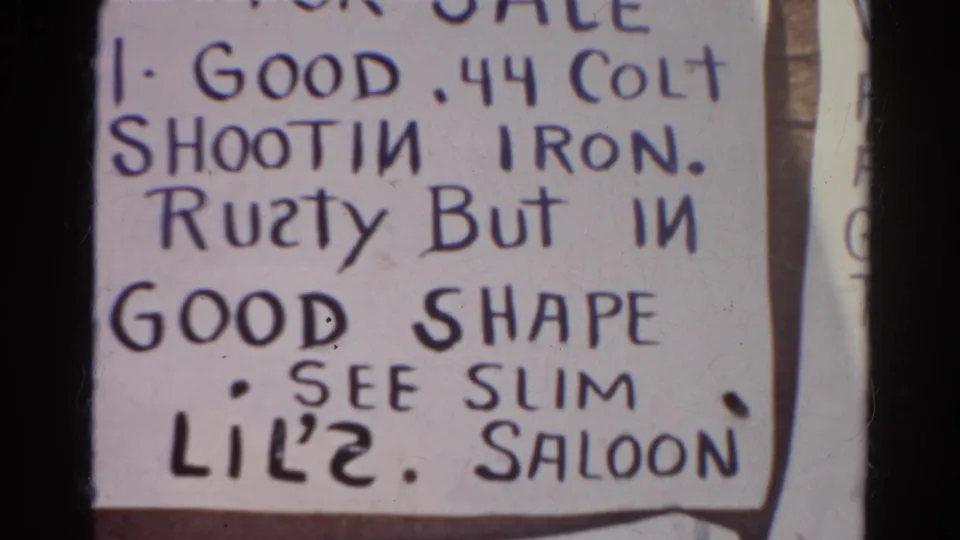 1966 8mm close-up emphasizing the lower lettering of the novelty Colt sale sign, including the instruction to see Slim at Lil's Saloon.
