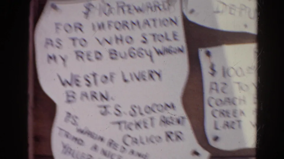 Soft 8mm frame from 1966 Silver Lake showing handwritten reward notices on a bulletin board, with motion blur and warm color.