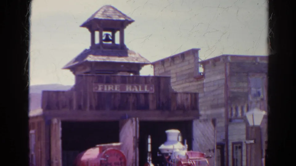 The camera holds on the Silver Lake Western-style fire hall, showing the bell tower, sign, open doorway, and red fire engine in soft 8mm color.
