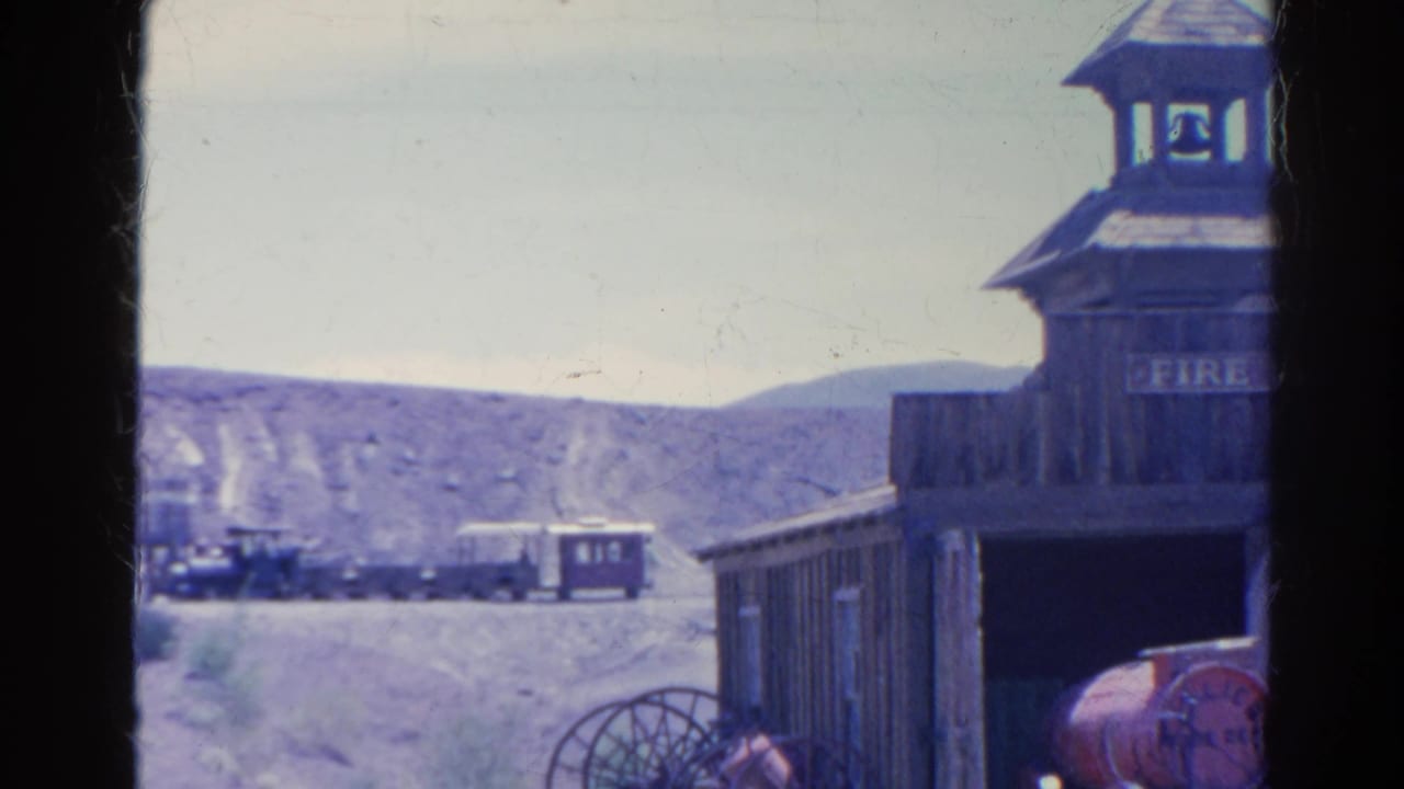 1966 8mm frame from Silver Lake, California showing a Western-style fire hall facade with bell tower, wagon wheel, distant train, and desert hills.