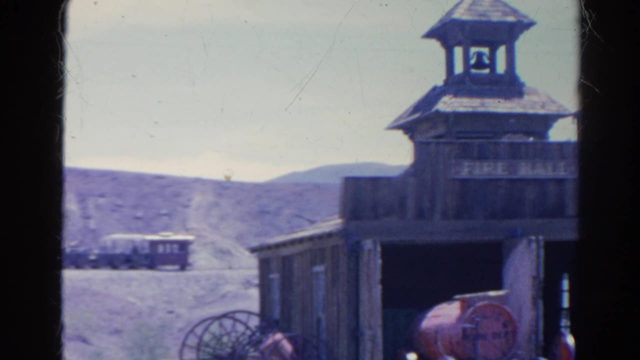 Wooden fire hall with FIRE HALL sign, open bay, red equipment, distant train, and desert hills.