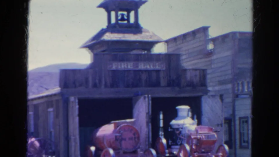 1966 Silver Lake frame showing the Western-style fire hall front with bell tower, FIRE HALL sign, open bay, firefighting equipment, and nearby wooden building.