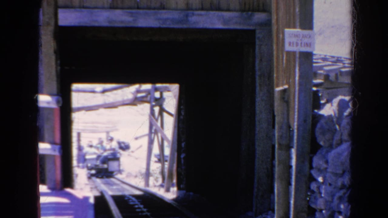 Tram tunnel entrance with warning signs, rails, stacked rockwork, and tram visible outside.