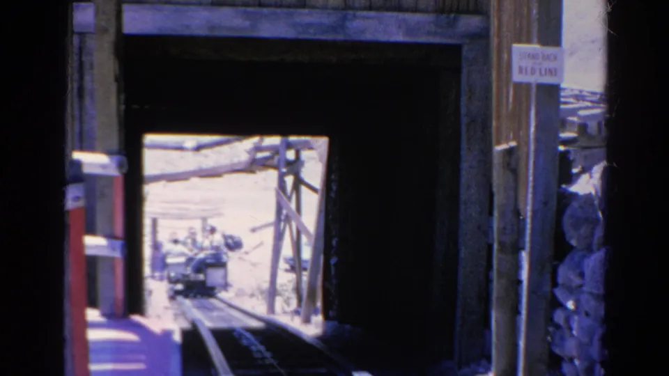 1966 Silver Lake 8mm frame showing the cable tram route through a shadowed tunnel toward a small passenger tram outside.