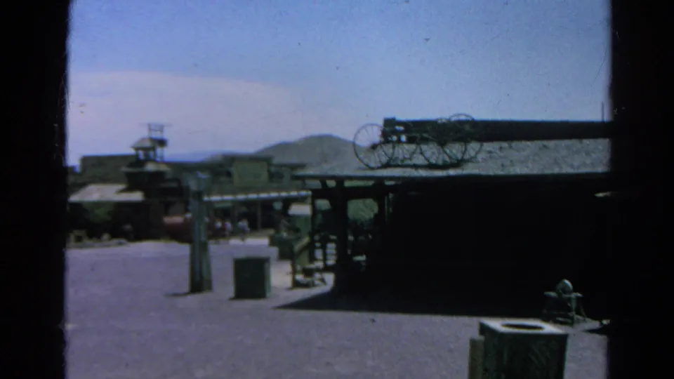 1966 Silver Lake frame showing rustic wooden structures, wagon wheels, open ground, and distant hills after the tram tunnel sequence.