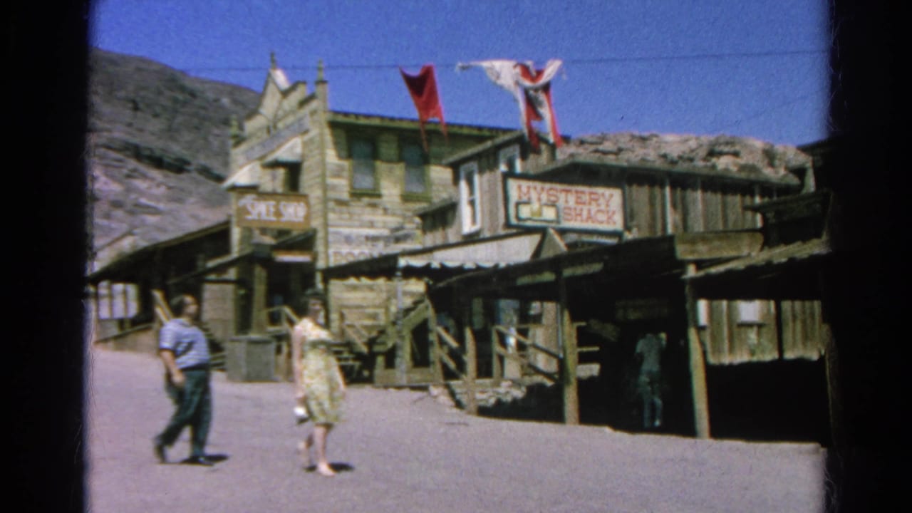1966 Silver Lake 8mm frame showing two adults walking by rustic wooden storefronts with Spice Shop and Mystery Shack signs.