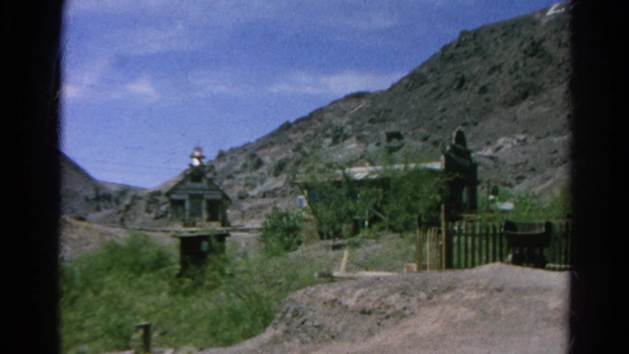 A small towered structure, fencing, shrubs, and hills appear beside an empty path.