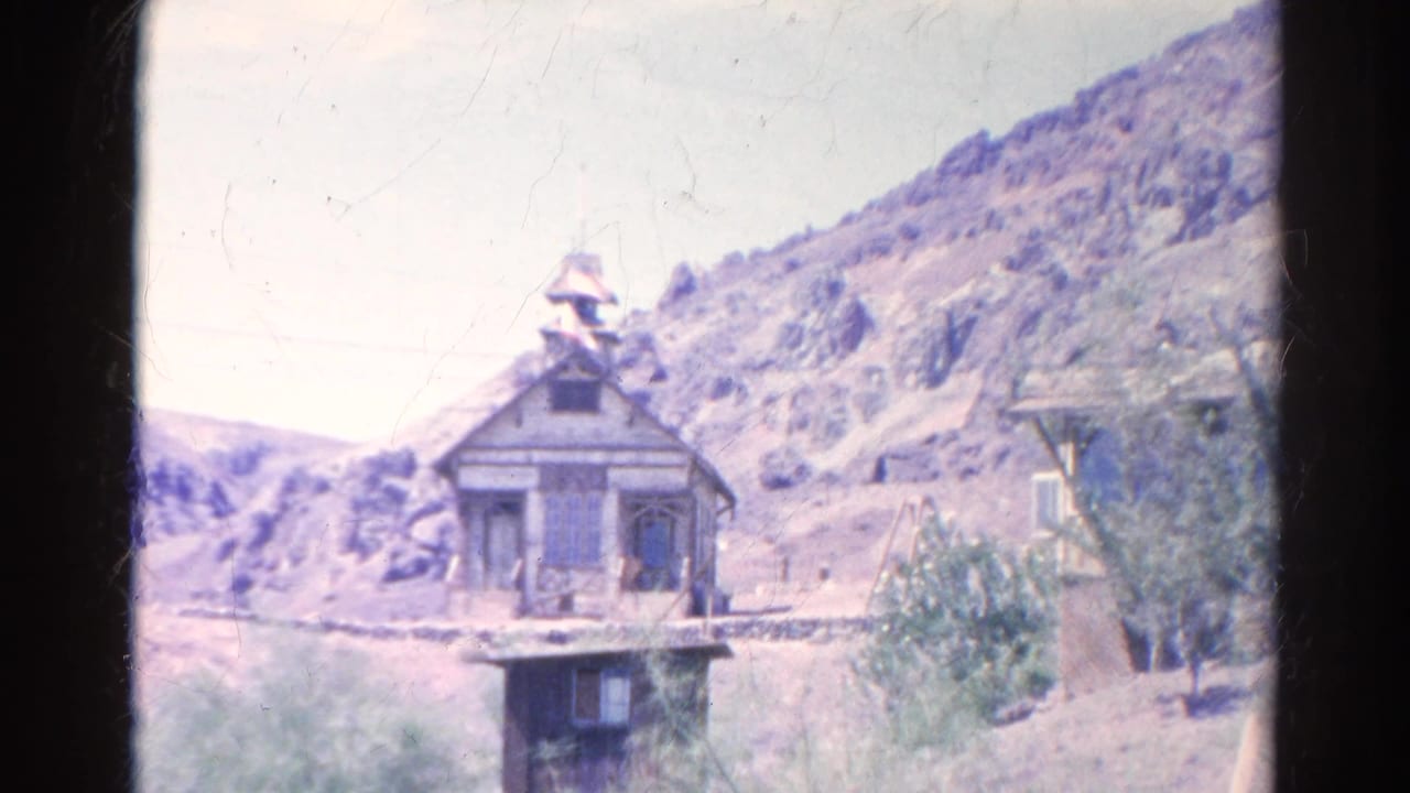 Wide view of a weathered wooden building with a bell tower in arid hills.