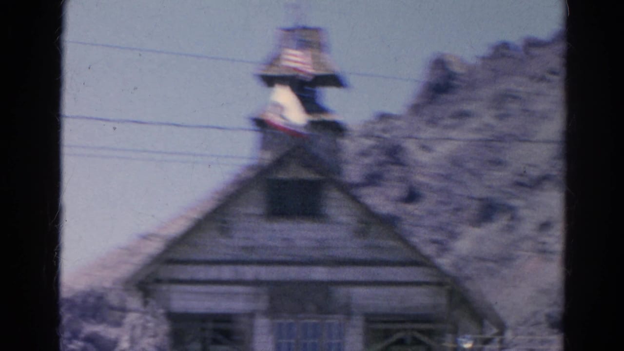 Blurred view of the same wooden building and flag below a rocky hillside.