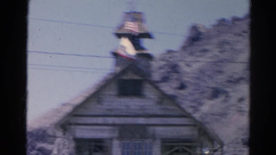 Soft 1966 Silver Lake frame with the rustic wooden facade, tower top, American flag, and pale rocky slope in the background.