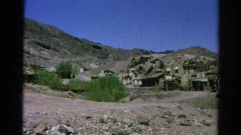 1966 Silver Lake home-movie frame showing rustic buildings spread across an arid rocky hillside with green scrub and clear sky.