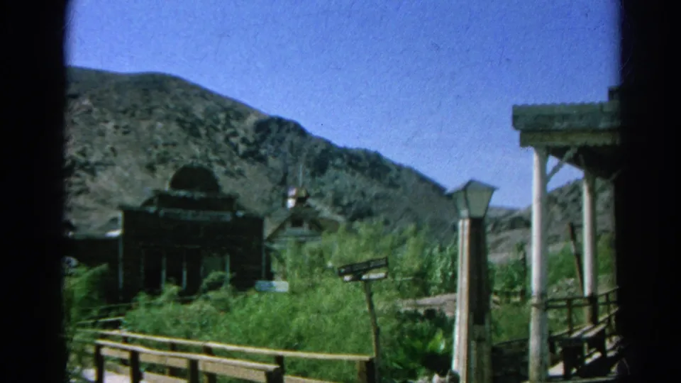 1966 Silver Lake, California home-movie still of a rustic church-like facade beside railings, brush, signs, and dry hills.