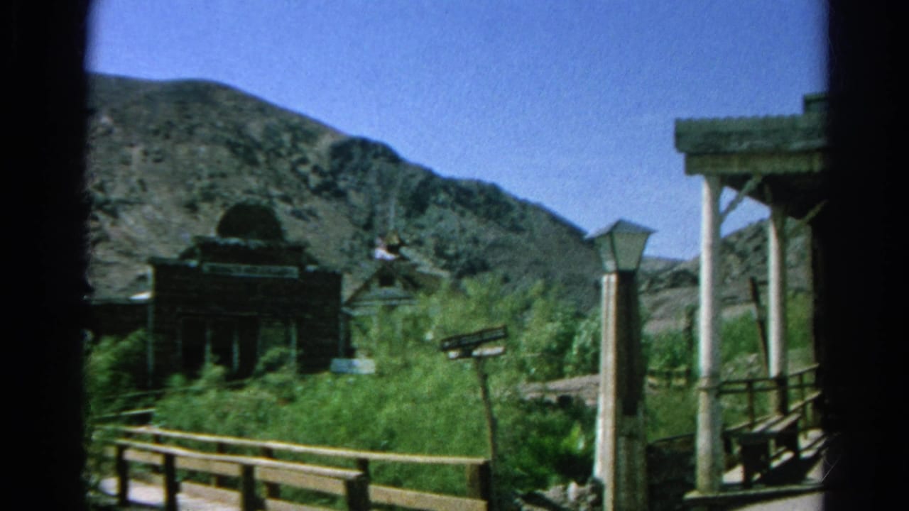 1966 Silver Lake frame with a dark wooden Western storefront, lamppost, shrubs, and arid hills behind it.