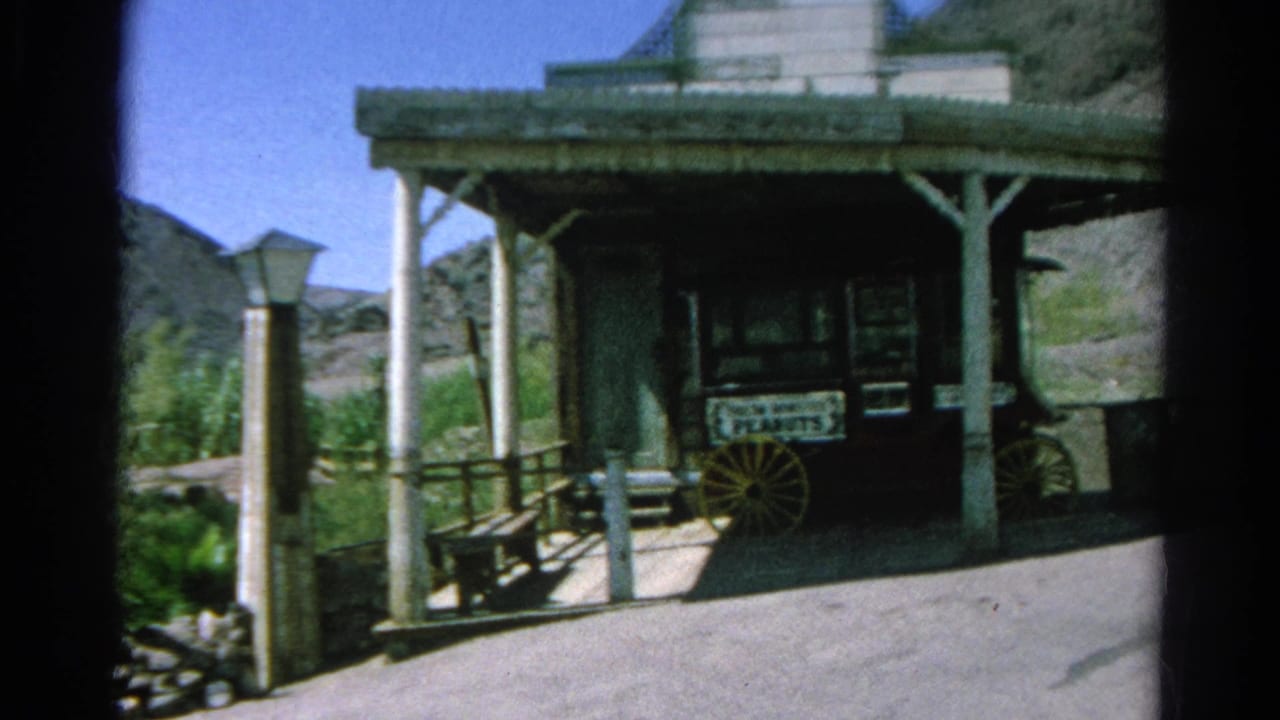 Covered wooden stand with wagon wheels and a Fresh Roasted Peanuts sign beside rocky landscaping.