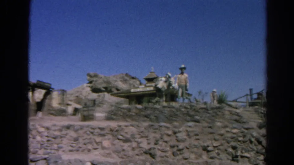 1966 Silver Lake home-movie view of a Western set with stonework, rocky landscaping, wagon, small structure, and standing figure.