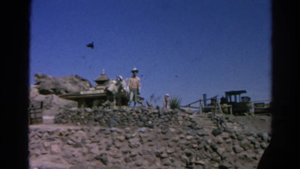 1966 Silver Lake frame showing a wider Western set view with stone wall, wagon, cowboy-hatted figure, railings, and a small cart at right.