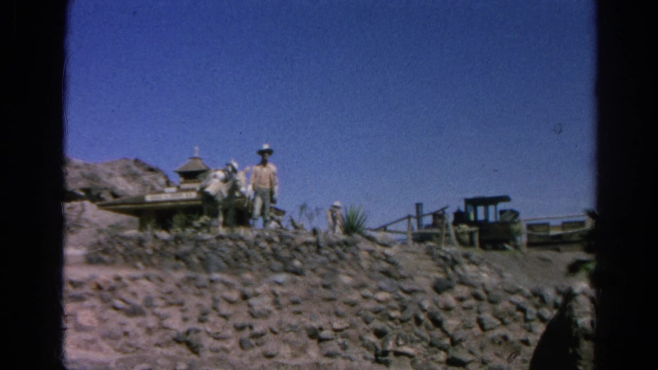1966 8mm frame from Silver Lake, California, showing a man on rocky ground beside Western-style structures and a small cart.