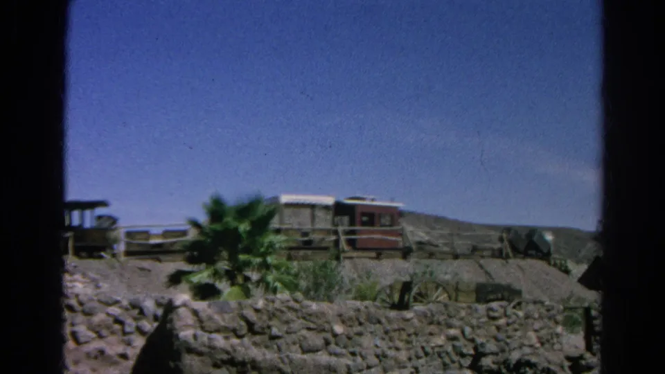 End frame of the 1966 Silver Lake 8mm pan with palm greenery, small rail cars, fencing, and sunlit rocky terrain.
