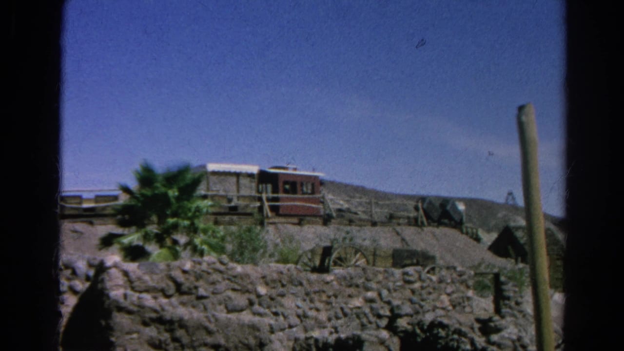 1966 Silver Lake, California 8mm frame showing rustic structures, a red railcar-like object, rocky terrain, and a palm tree.