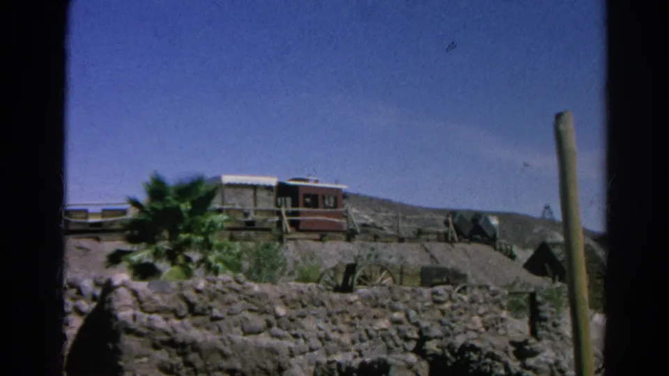 1966 Silver Lake, California 8mm frame showing rustic structures, a red railcar-like object, rocky terrain, and a palm tree.