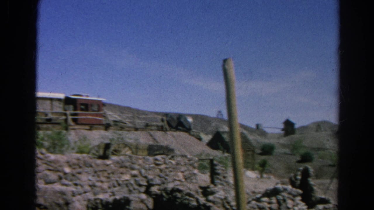 Weathered structures and rocky desert ground with a tall pole in the foreground.