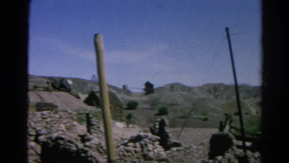 1966 Silver Lake, California pan frame showing dry hills, utility poles, rockwork, scrub vegetation, and a small dark structure.