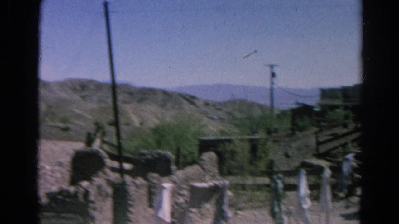 Desert ghost town ruins with distant visitors and hills beyond.