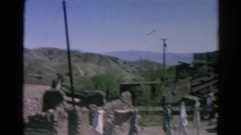 1966 8mm view of Calico-area ghost town ruins with a few distant visitors, desert hills, and soft home-movie framing.