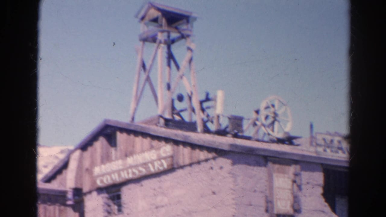 1966 8mm frame of the Maggie Mining Company commissary facade at Calico, with a wooden headframe and mining wheels on the roofline.