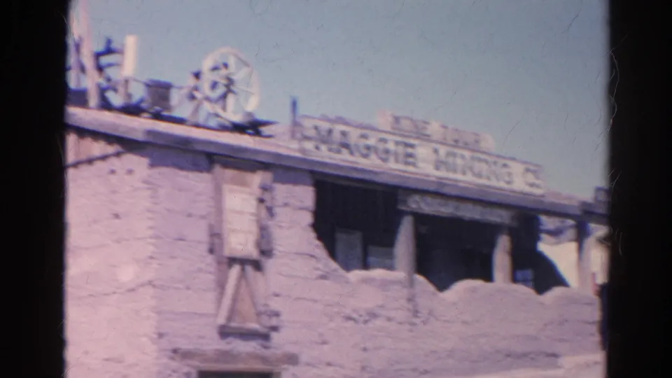 1966 8mm view of the Maggie Mining Company building, showing faded roof signage, shaded porch openings, and rough exterior walls.
