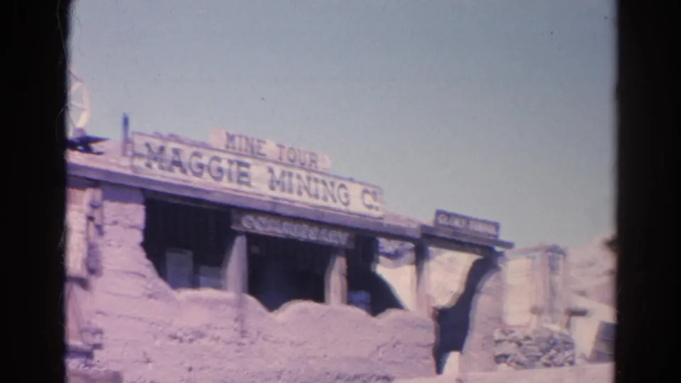 1966 8mm frame from Silver Lake, California showing the Maggie Mining Co. mine tour entrance with rustic signage, rockwork, and a water wheel.