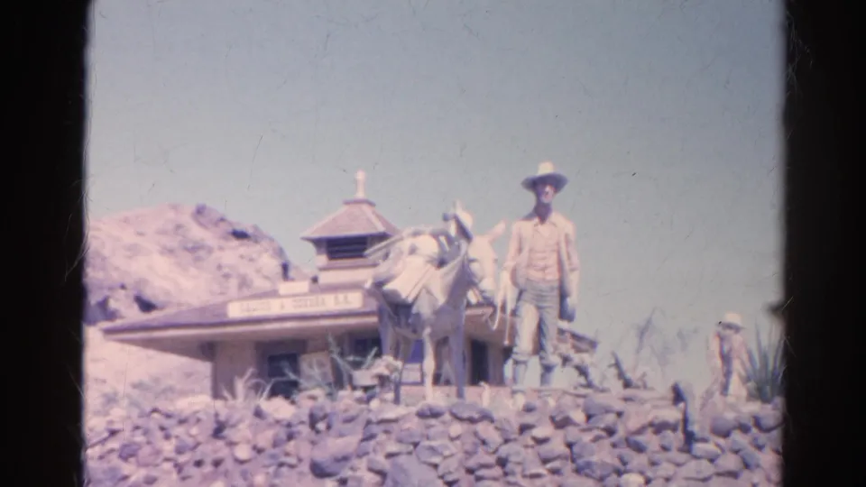 1966 8mm frame showing the Western-themed cowboy and donkey display at the Silver Lake attraction, with rockwork and a small building behind.