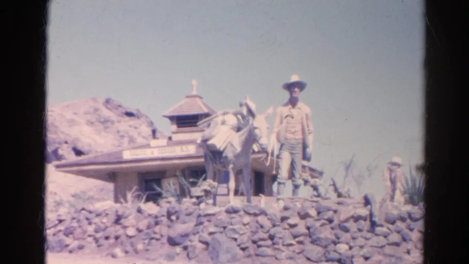 Final 1966 Silver Lake, California frame of the cowboy-and-donkey display, with a small themed building, rocks, and pale blue sky.