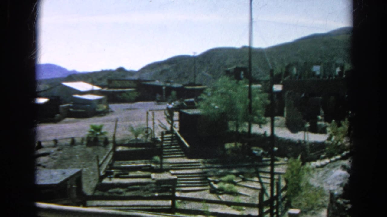 Elevated view of a dry mountain settlement with stairs, fences, utility poles, and low buildings.