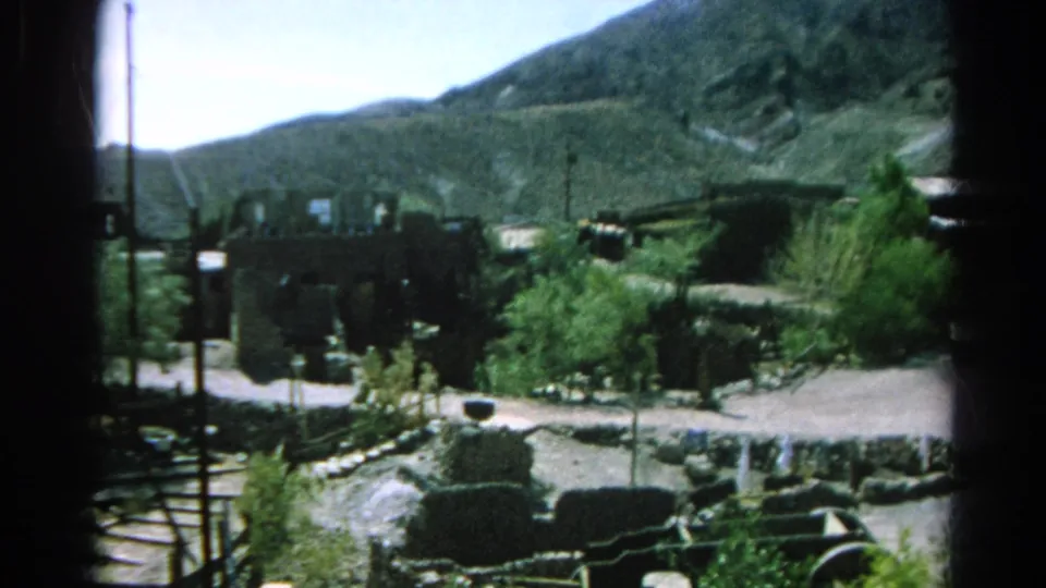 1966 Silver Lake, California 8mm still showing weathered low structures, trees, stone borders, a pale road, poles, and dry mountain terrain.