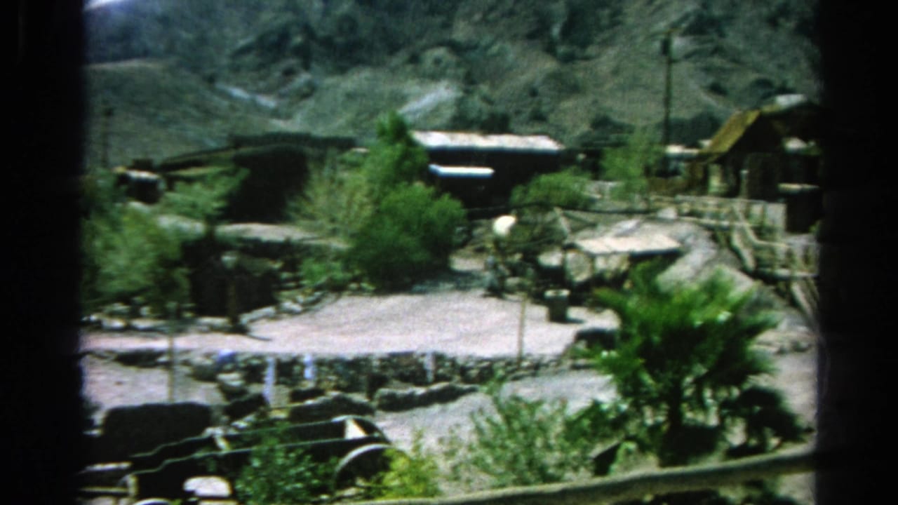 Rocky Western-style town viewed through dark window framing, with buildings, paths, and greenery.
